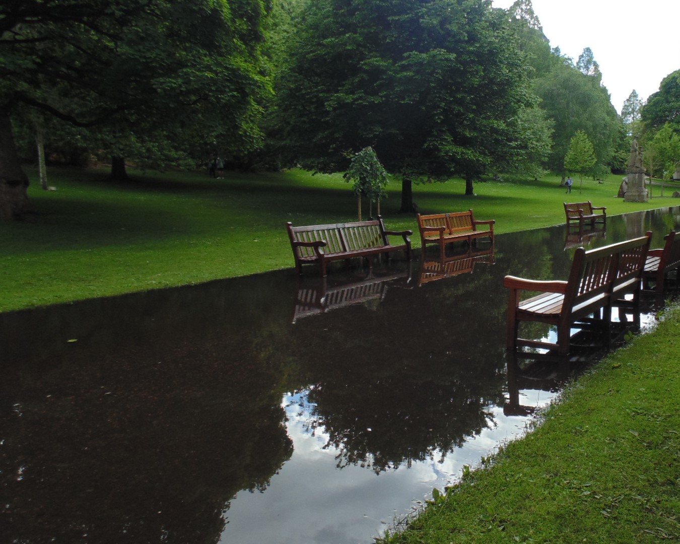 a photo of benches sitting in water that has flooded the path. the sky is clearly reflected in it