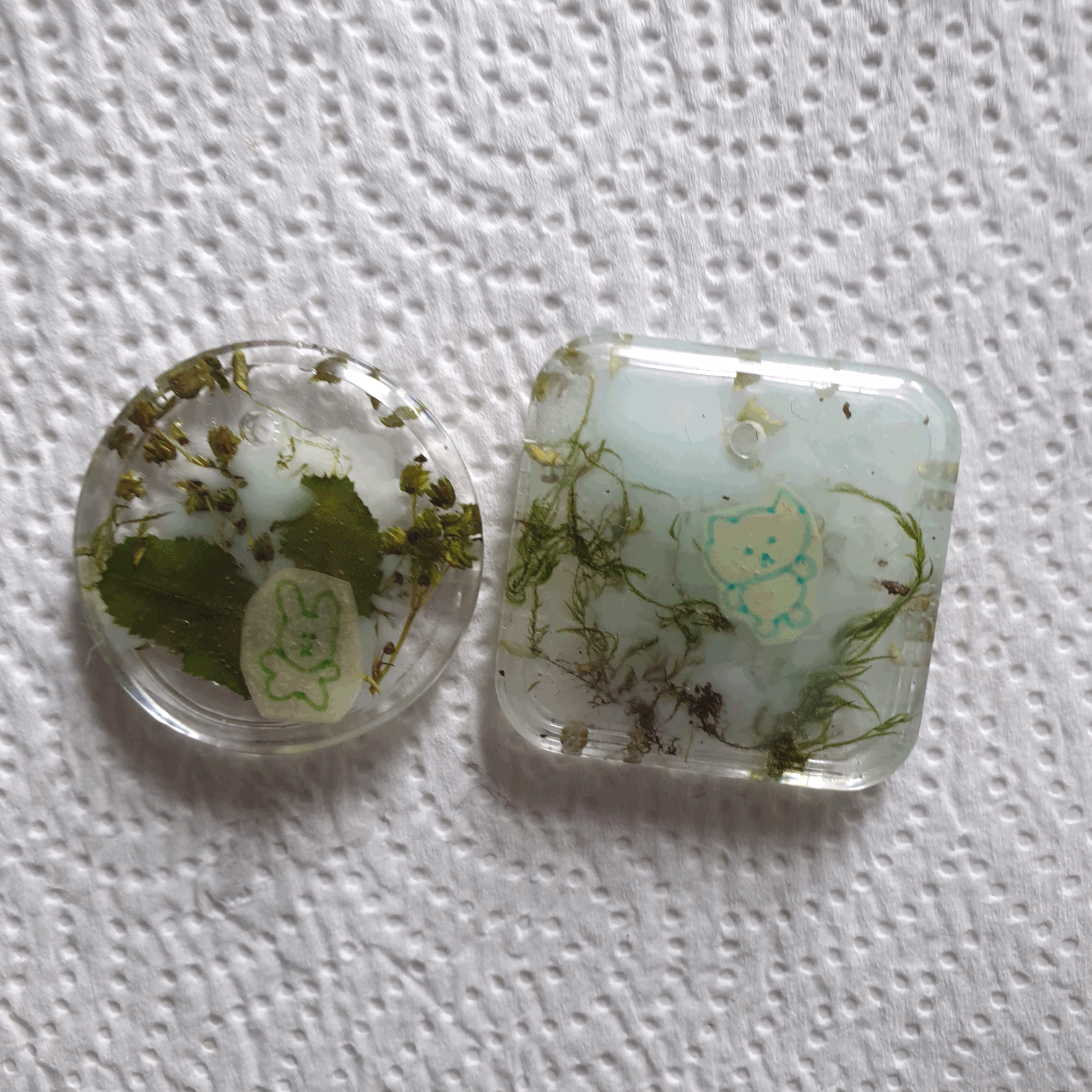 2 resin keychains with plants and a small doodle on paper inside, one cat and one bunny.