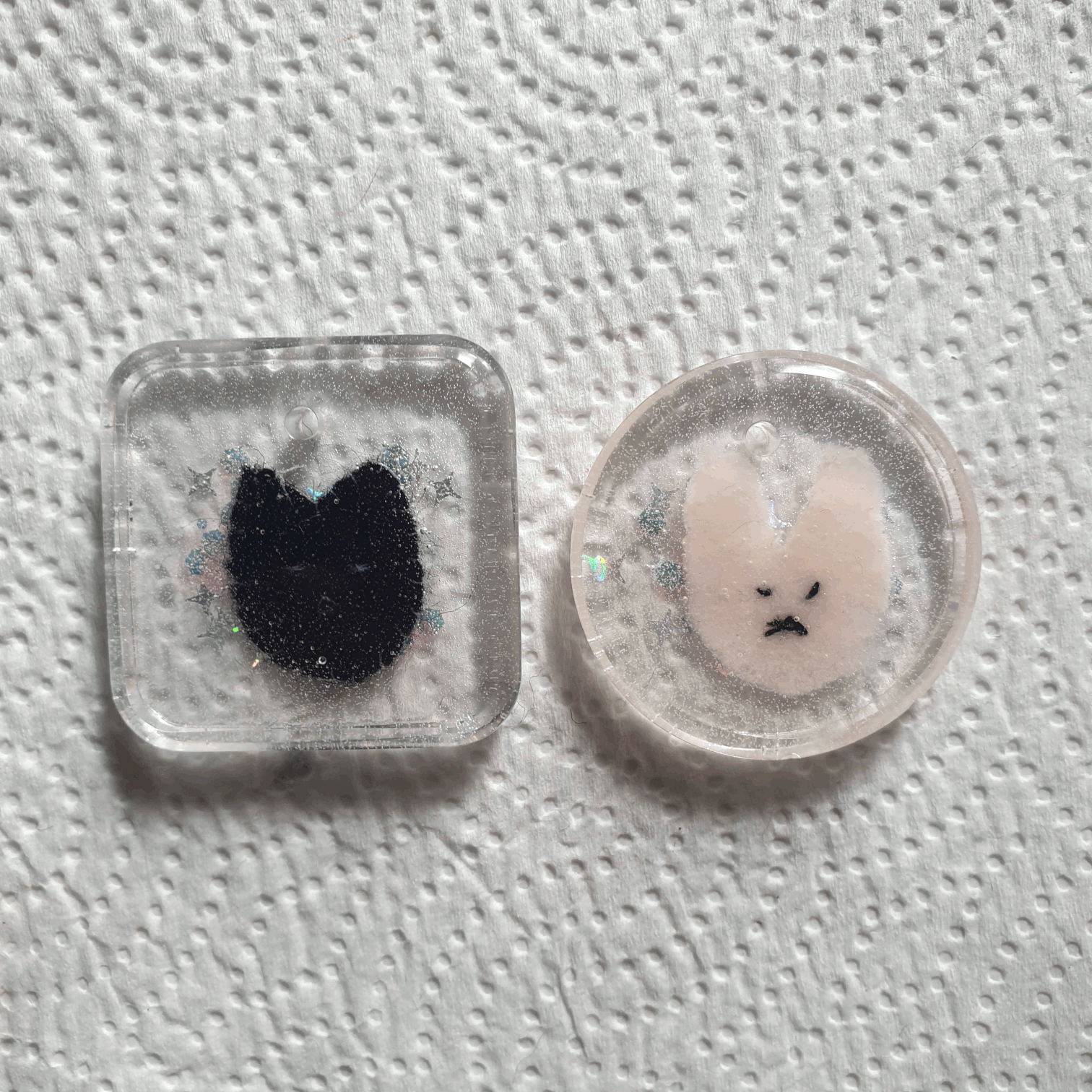 2 resin keychains with felt characters inside, one pink bunny with white stitching (that isn't clearly visible) and a black face. one black cats with white stitching - the face isn't big enough to be clear